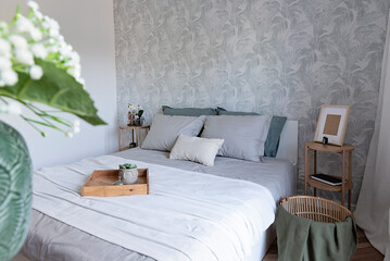 Interior of a bedroom with comfortable bed with pillows and bedding. Cozy room with stylsih wallpaper on the wall, decoration and flowers. Hotel with bed and furniture.