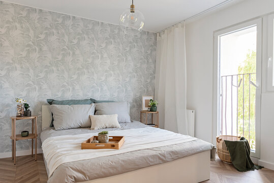 Cozy interior of bedroom with bed with pillows and modern wallpaper on the wall. Home interior with light and comfort to sleep.