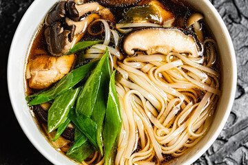 Mushroom soup udon noodles with fresh green onions against a black design board, a traditional...