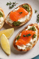 Delicious bruschettas with cream cheese, salmon and pesto sauce on plate, closeup