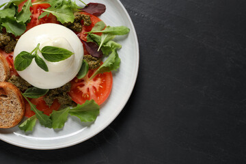 Delicious burrata salad with tomatoes, arugula and pesto sauce on black table, top view. Space for text
