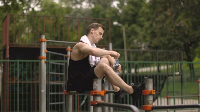 Little break. Young athletic guy with muscular body, sportsman and fitness model, strong man sitting on parallel bars. Athletic body shape, guy relax at outdoor gym.