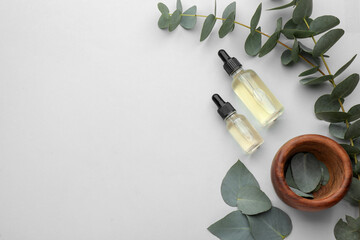 Bottles of eucalyptus essential oil and plant branches on white background, flat lay. Space for text