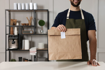 Worker with paper bag at counter in cafe, closeup. Space for text