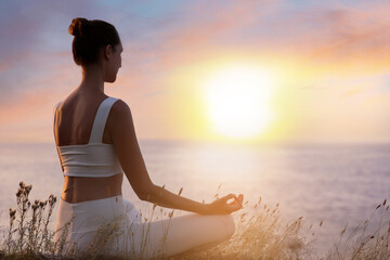 Fototapeta na wymiar Woman meditating near sea at sunset. Practicing yoga