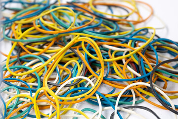 Pile of colored stationery rubber bands yellow blue red green black colors on white background close-up