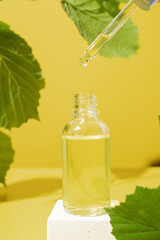 Mock up glass dropper bottle on a white podium on yellow background with leaves. Hard shadows. Cosmetic facial skin care and spa. Natural treatment concept.