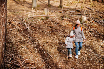 Mother with daughter wear jacket and hat in early spring forest.