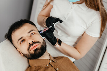 Fototapeta premium Stylish bearded man visiting aesthetic clinic, getting lips filler, closeup. Man having beauty injection at male spa salon. Anti-aging treatment for men concept