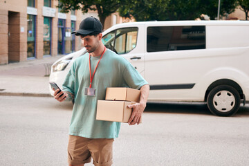 Letter carrier checks an order with his mobile phone with a van in the background