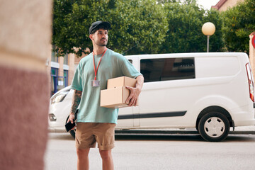 A letter carrier holds boxes during a delivery with a van in the background