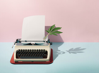 Pastel pink and blue background against retro vintage typing machine, paper and marijuana in crystal glass. Creative retro concept. Retro futurism.