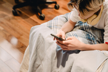 White teenage boy using cellphone while lying in bed at home