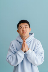 Brunette adult asian man praying and keeping palms together