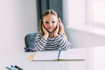 Naklejka premium Unhappy little Caucasian girl child sit at table at home feel lazy unmotivated doing homework assignment. Upset distressed small kid prepare school task, learn study with books. Education concept.