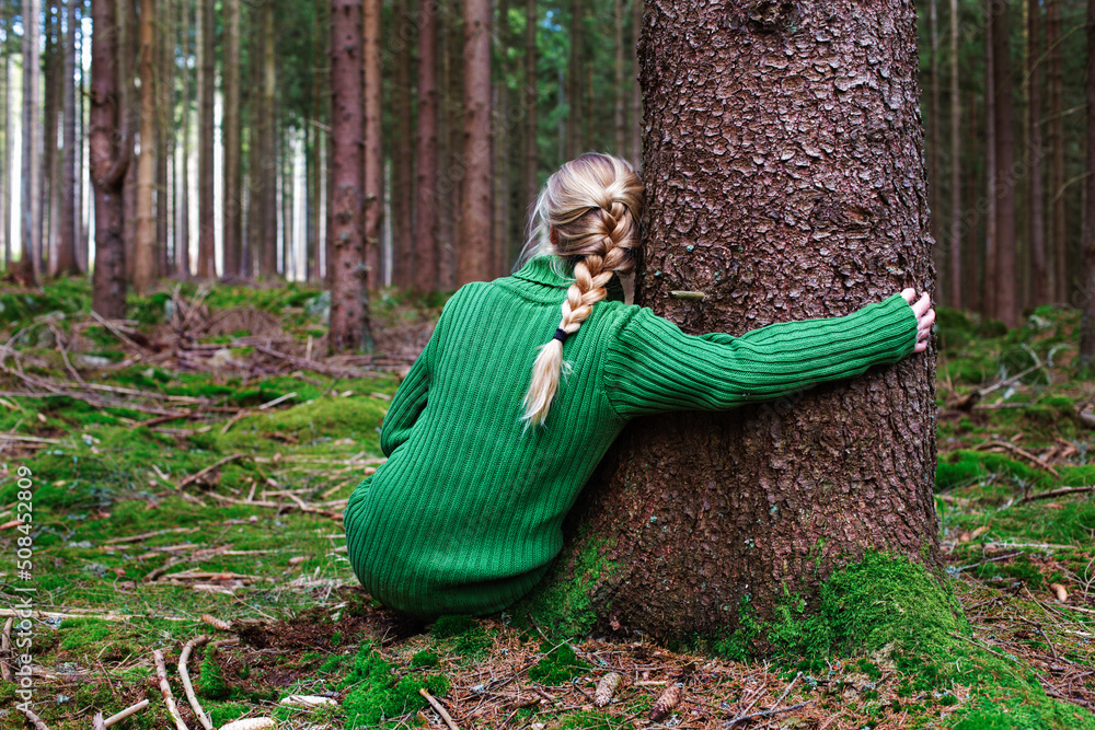 Wall mural woman sitting in forest hugging tree, enjoys the silence and beauty of nature.