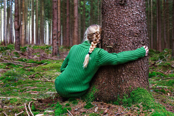 Woman sitting in forest hugging tree, enjoys the silence and beauty of nature.