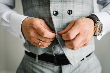 Man fastens the buttons. The groom in a suit, shirt standing in room. Close up.