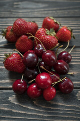 closeup of ripe cherry and red strawberry on wooden background