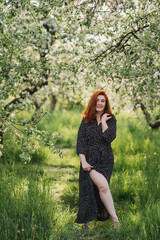 Portrait of gorgeous middle aged woman in casual dress relaxing in a blooming spring garden. Happy senior woman smiling and looking at camera. Red-haired mature lady posing outdoors in a spring day.