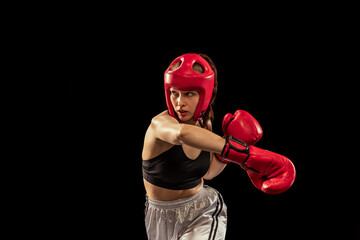 Professional female boxer in boxing gloves and helmet training isolated on dark studio background....