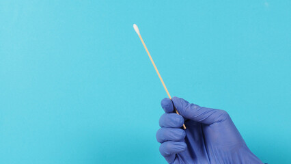 Cotton stick for swab test in hand with violet medical gloves or latex glove on blue background.