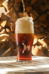 Glass of beer on a blurred background of firewood. A full glass of fresh beer. Beer glass and timber. Shallow depth of field