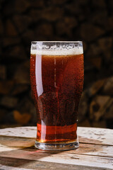 Glass of amber beer on a blurred background of firewood. Full glass of fresh beer on a wooden old table. Shallow depth of field