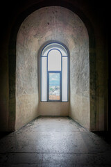 Large antique window in an 18th century castle  that shows a beautiful natural landscape with branches, leaves, trees and a cloudy blue sky and mountains