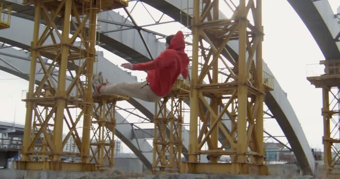 Young sporty guy running, doing cartwheel and performing epic backflip while parkouring at construction site