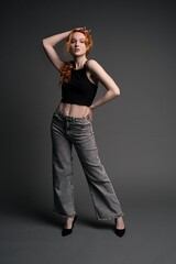 Confident young woman standing in gray studio with hand on waist