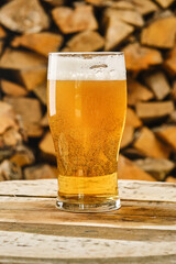 Glass of light beer on a blurred background of firewood. Full glass of fresh golden beer. Beer glass and timber. Shallow depth of field