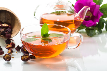 brewed rosehip tea in a glass teapot with rosehip flowers and mint
