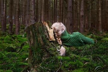 Blond woman sitting in green forest enjoys the silence and beauty of nature.