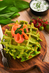 Green Belgian waffles. Spinach or wild garlic or pesto waffles with red salmon and cream sauce on black plate over dark rustic wooden background. Delicious breakfast, snack, brunch. Mock up