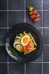 Savory waffles. Breakfast green waffles wild garlic or spinach with egg, tomato, salmon on wooden plate for breakfast on old black tile table background. Light dinner, lunch or breakfast. Top view.