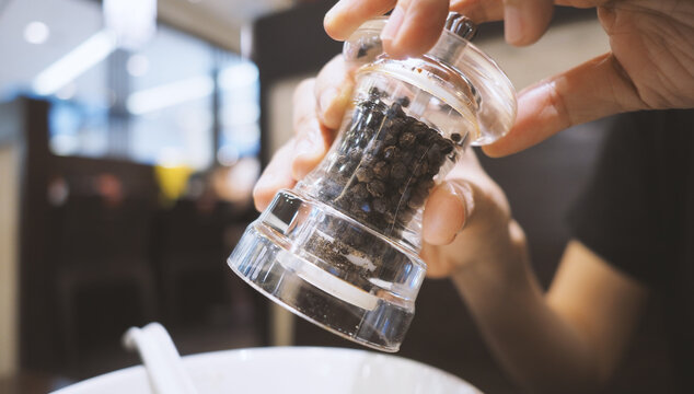 Clear color glass and Thailand black pepper mill or grinder in hands that twisting the bottle and pouring or adding small pieces of spices to plate or bowl for a better taste in the meal.