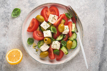 Greek salad. Fresh Greek salad with fresh vegetables, tomato, cucumber, green olives and feta cheese on old grey concrete table background. Top view.