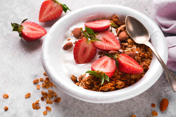 Granola. Bowl of homemade granola with yogurt and fresh berries strawberry for breakfast in a white bowl on old gray concrete background table background. Top view flat lay background.