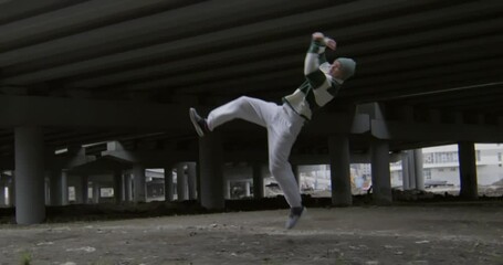 Male parkour athlete performing three epic side flips in slow motion under urban bridge - Powered by Adobe