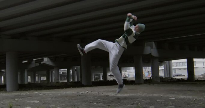 Male parkour athlete performing three epic side flips in slow motion under urban bridge