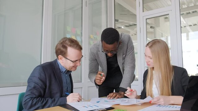 Ethnic diverse team brainstorming in office, discussing startup project. African black man writes idea on colorful stickers on the wall, then they talk and support each other. Young business people 