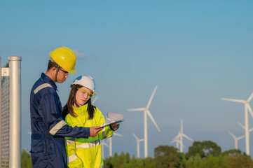 Two engineers working and holding the report at wind turbine farm Power Generator Station on mountain,Thailand people,Technician man and woman discuss about work