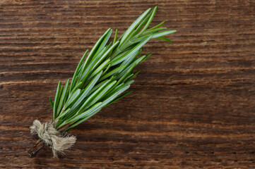 Rosemary plant on wooden background from above, bundle of fresh herbs with copy space for text.