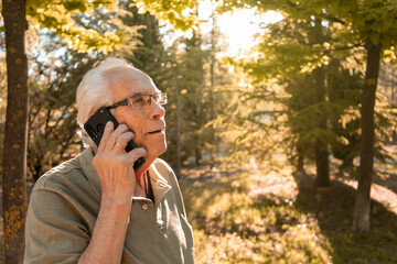 Retrato de hombre mayor llamando por teléfono móvil, en la montaña, en día soleado. Fotografía...