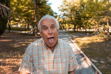 Hombre maduro, con gesto divertido, con la lengua fuera, en el parque en día soleado. 