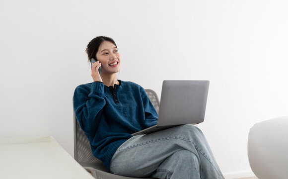 Portrait of smiling beautiful business asian woman using laptop computer and calling byh mobile phone from home concept