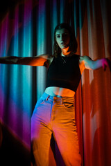 Fototapeta na wymiar Young and sexy woman with wearing jeans and black t-shirt posing in colorful neon light