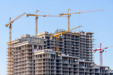 Construction cranes near the facade of a house under construction. modern building industry. Sale and rental of real estate.
