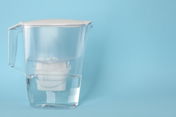 Filter jug with purified water on light blue background. Space for text